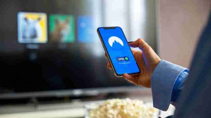 Person using VPN on smartphone while watching smart TV at home., tags: google pixel mit - pexel